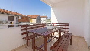 Een balkon met een houten tafel en bankjes, een plant in een pot en een uitzicht op gebouwen op de achtergrond.