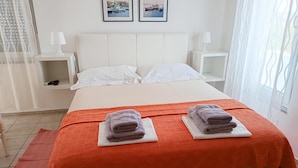 En snyggt bäddad säng med vita lakan, två kuddar och två hopvikta handdukar på vita underlägg.