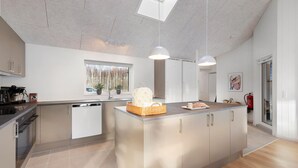 Una cocina moderna con una isla central, lavavajillas y una ventana con vistas a árboles.