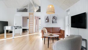 Una sala de estar moderna con un sofá, una mesa de centro y un televisor. Se ve una escalera que sube a una zona de altillo.