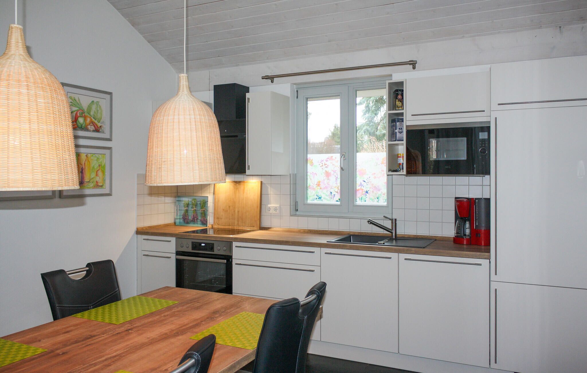 A modern kitchen with white cabinets, a wooden dining table, and pendant lights.