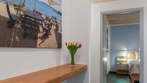 Una camera d'albergo con uno scaffale in legno, un quadro raffigurante una spiaggia e un vaso di tulipani.
