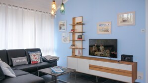 Un soggiorno moderno con un divano componibile, un tavolino, una TV e un mobile contenitore in legno con ripiani.