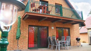 A two-story house with a balcony, a patio with chairs and a table, and a barbecue grill. - Cozy home in Röbel with lake view (Röbel)