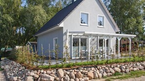 Ett tvåvåningshus med en grå fasad, ett mörkt tak och en inglasad veranda.