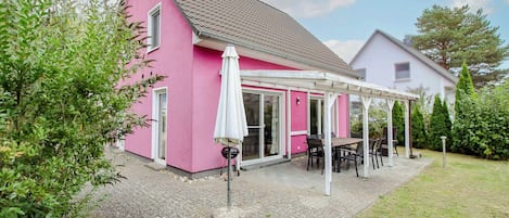 A pink house with a covered patio, a satellite dish, and a garden.