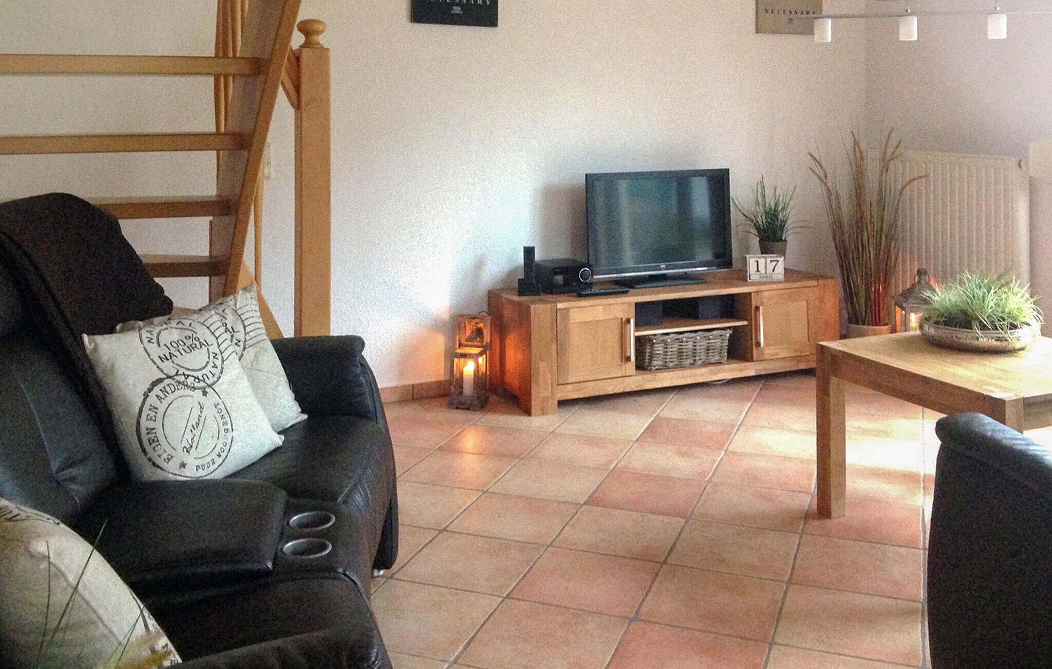 A living room with a wooden TV stand, a sofa with a cushion, a small table, and a potted plant.