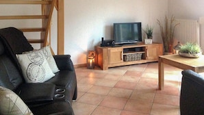 Una sala de estar con un mueble de televisión de madera, un sofá con un cojín, una mesita y una planta en maceta.