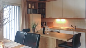 Una cocina moderna con comedor, que incluye una mesa de madera, sillas negras, una planta y una botella de vino.
