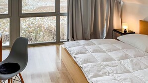 Een slaapkamer met een bed, een stoel, een nachtkastje met een lamp en een raam met gordijnen.