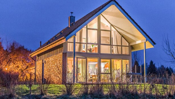 Een modern huis met grote ramen, een stenen gevel en een schuin dak.