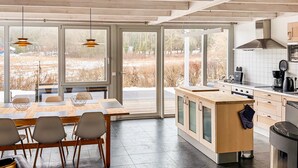 Een moderne keuken met een centraal eiland, grote ramen en een zithoek met stoelen.