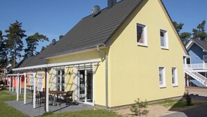 En gul bygning med saddeltag, en overdækket terrasse med udendørs siddepladser og en trappe til en øvre etage.