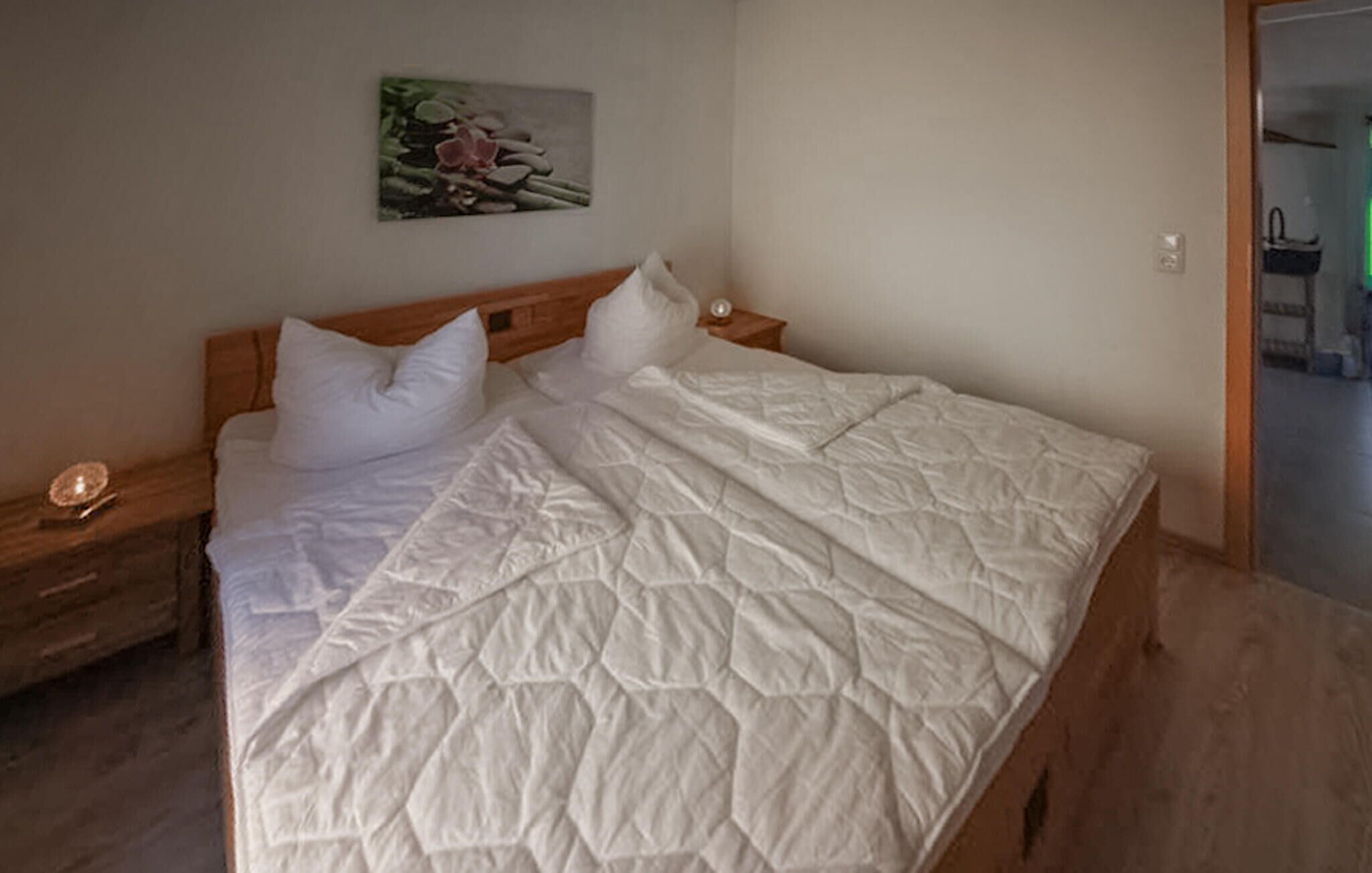 Een opgemaakt bed met een witte deken, twee nachtkastjes en een aan de muur hangend schilderij.