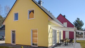 Et gult hus med et rødt afsnit, en overdækket terrasse og en bil foran.