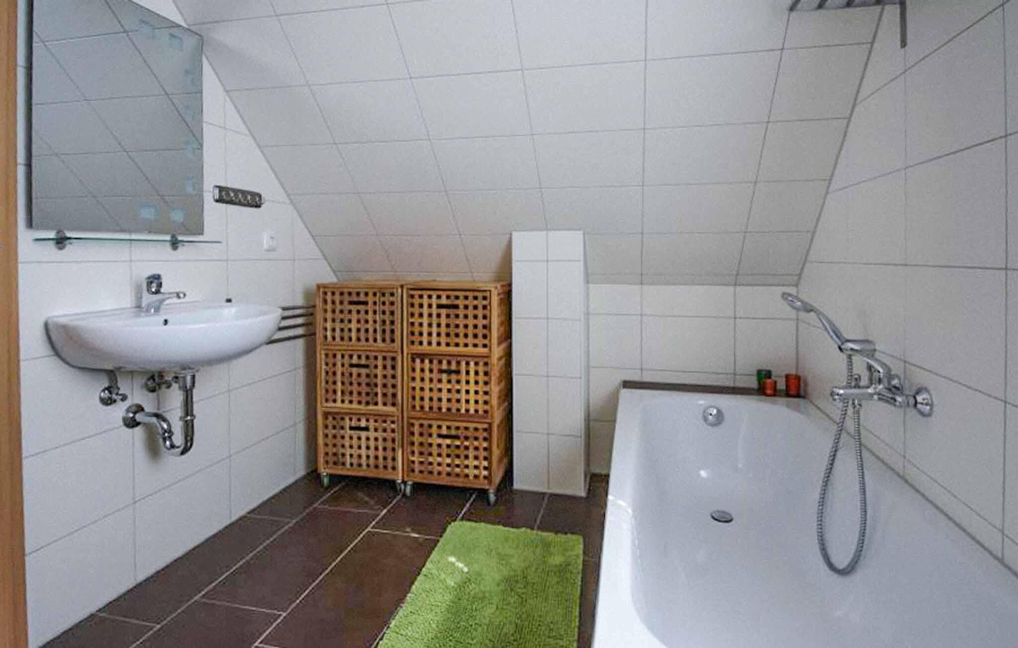 Un baño con lavamanos blanco, espejo y bañera. Hay una alfombra verde en el suelo.