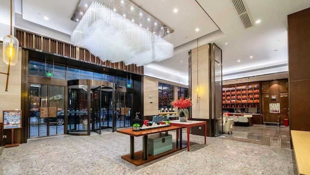 Un vestíbulo moderno con una mesa central, puertas de vidrio y una lámpara decorativa.