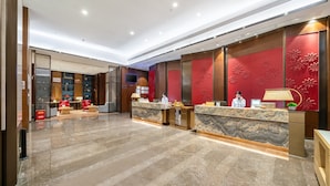 Zona de recepción de hotel con suelo de mármol, decoración floral roja en las paredes y diseño moderno.