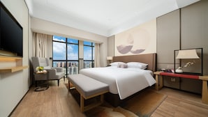 Habitación de hotel moderna con una cama grande, un escritorio, una silla, un televisor y vistas a la ciudad.