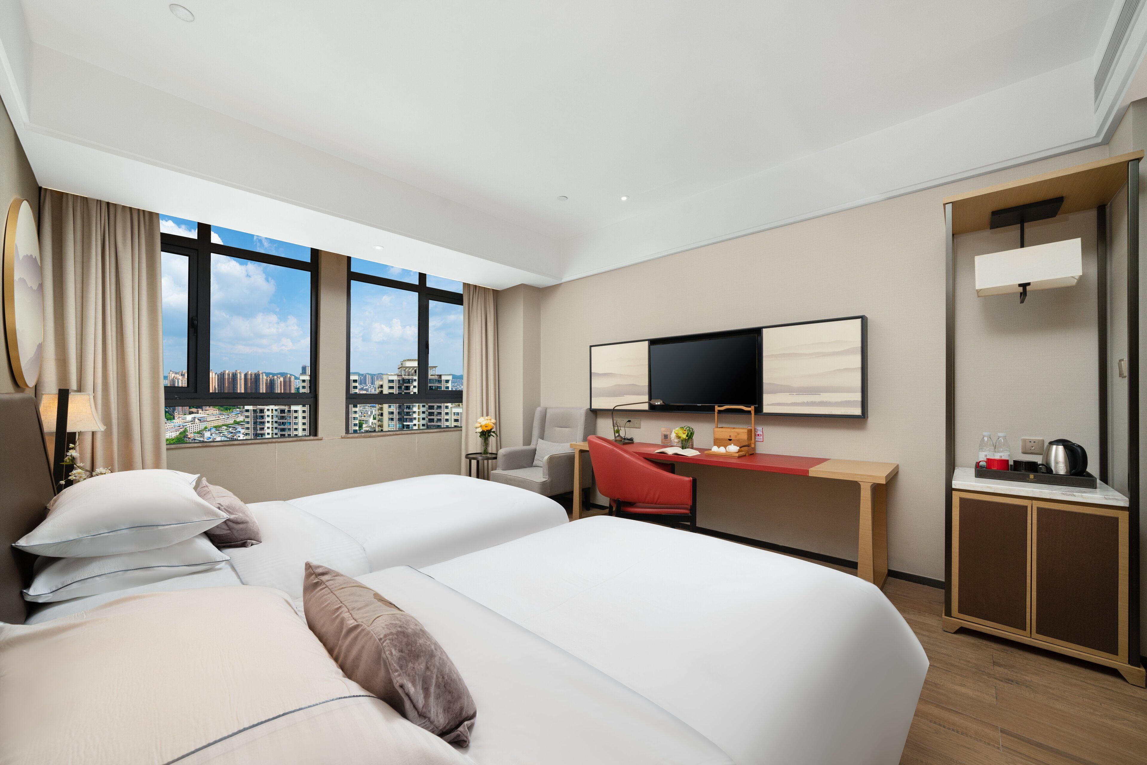A hotel room with two beds, a desk, a TV, and a view of the city.