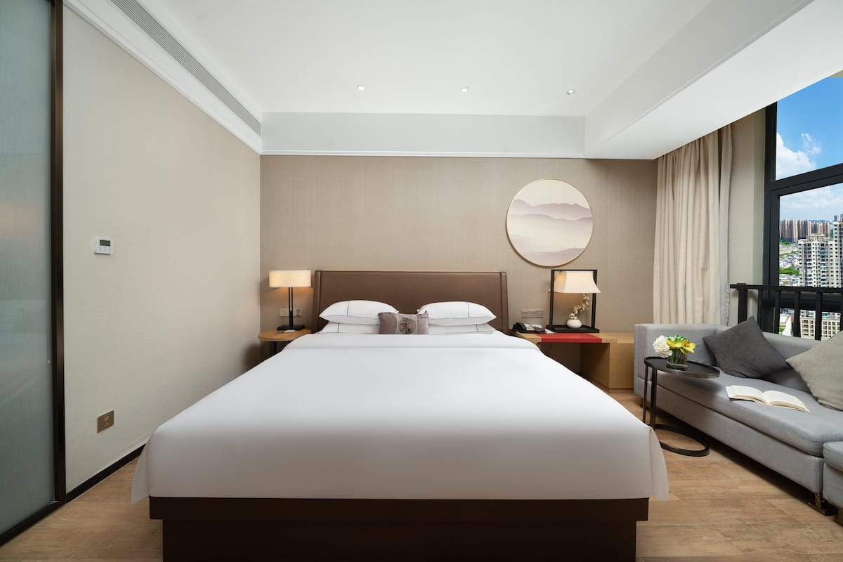 Habitación de hotel moderna con una cama grande, lámparas de noche, un sofá y vistas a la ciudad.