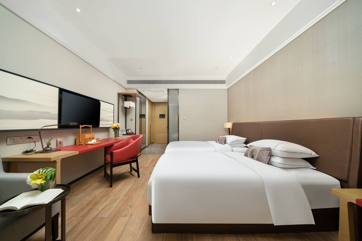 Habitación de hotel moderna con una cama grande, un escritorio con silla, televisión y baño visible a través de una puerta abierta.