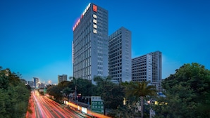 Un hotel de gran altura con varios pisos, un letrero llamativo en la fachada y vistas del entorno urbano con árboles y una calle concurrida con estelas de luz.