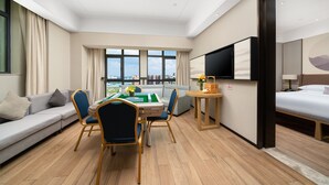 Una habitación de hotel moderna con sofá, una mesa de comedor con sillas, un televisor montado en la pared y una cama.