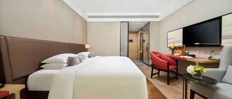 A modern hotel room with a large bed, a desk, a TV, and a red chair.
