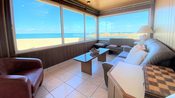 Ein Zimmer mit großem Fenster mit Blick auf einen Strand, einer Couch, einem kleinen Tisch und einer Lampe.