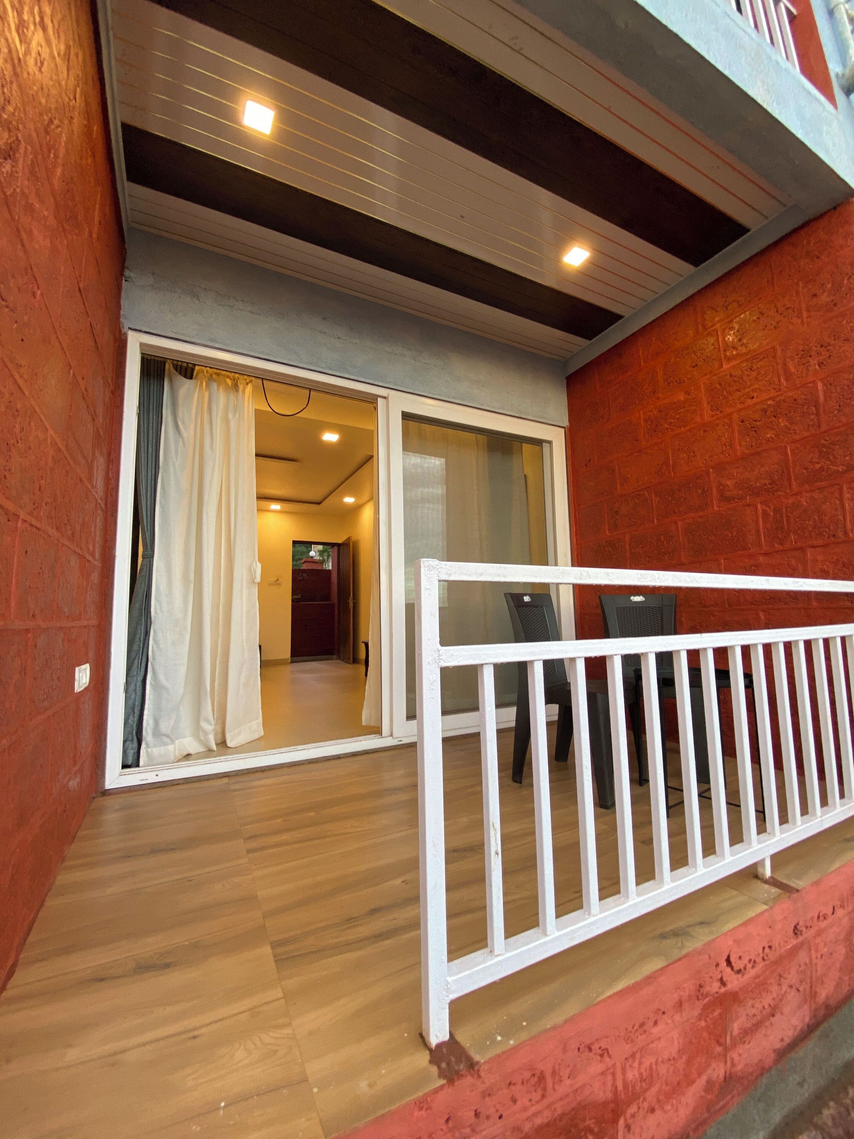 Un balcón con barandilla blanca, piso de madera y pared de ladrillo rojo.