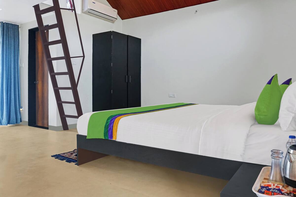 A bedroom with a bed, a wardrobe, a ladder, a tray with drinks and snacks, and an air conditioner.