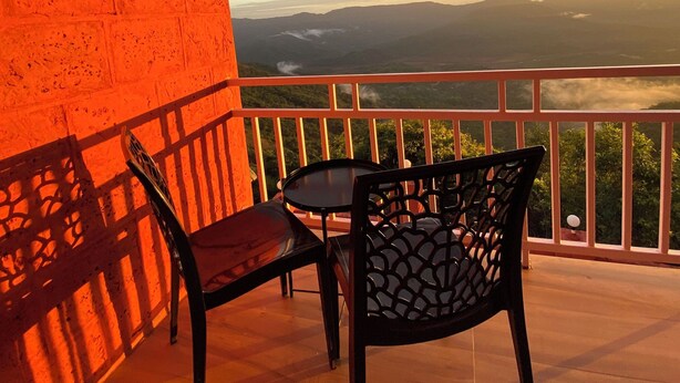 A balcony with a view of a mountain range, two chairs, and a table. - BLOOMS AND BERRIES AGRO TOURISM (Kalamgaon kalamkar)
