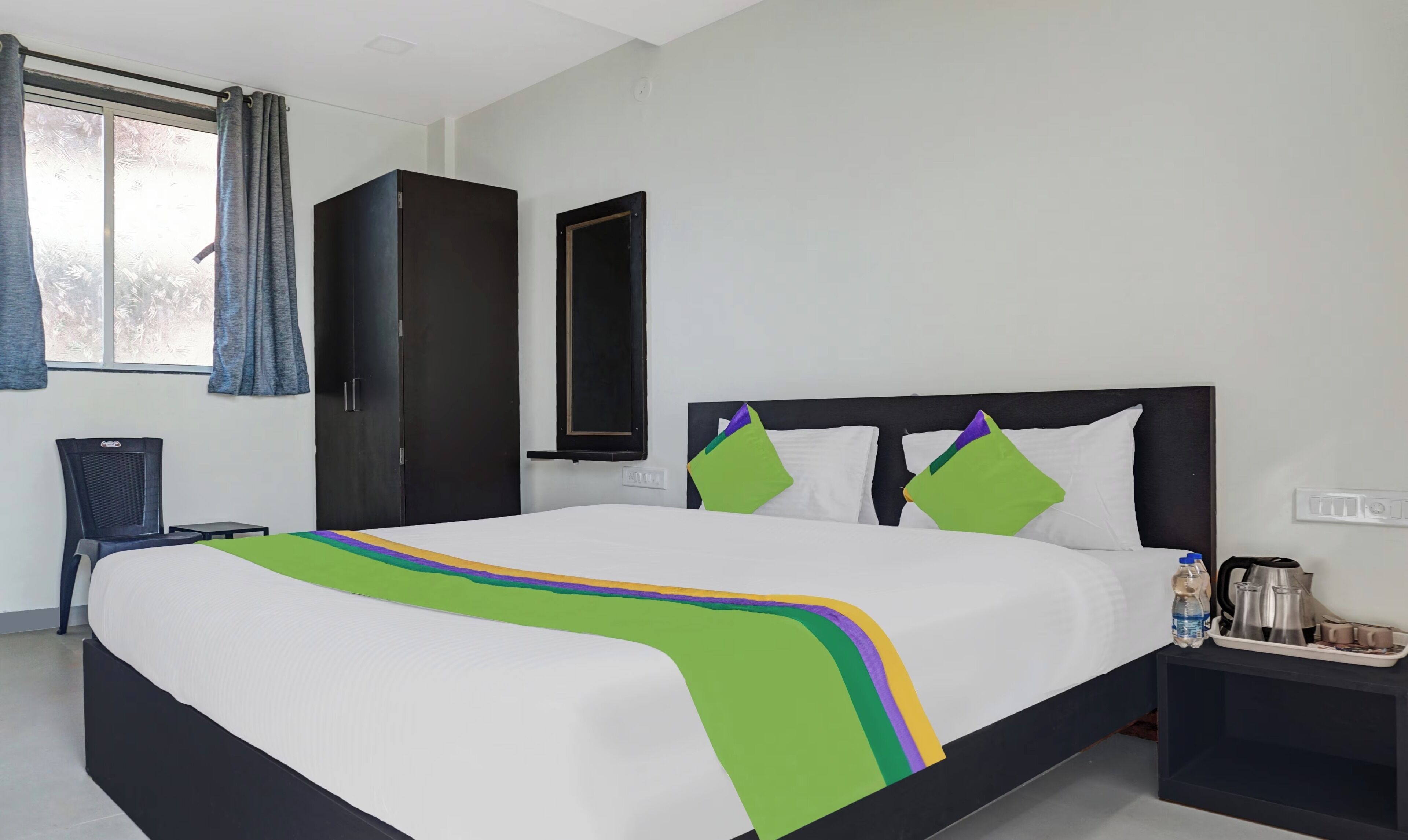Ein Hotelzimmer mit einem Bett, einem Nachttisch, einem Sessel, einem Kleiderschrank und einem Fenster mit Vorhängen.