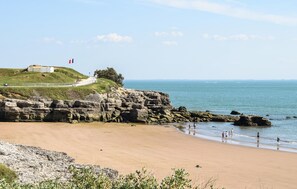 A coastal landscape with a sandy beach, rocky cliffs, and a flag on a hill. - Cozy home in Chenac-Saint-Seurin-d' (Chenac-Saint-Seurin-d')