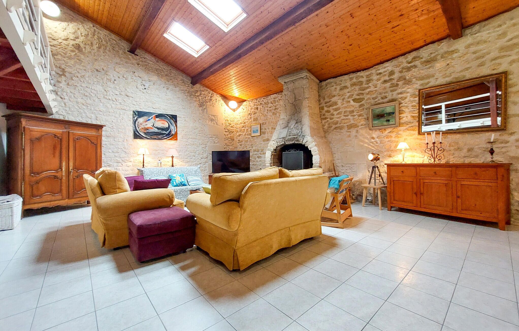 A cozy living room with a stone wall, wooden ceiling beams, a fireplace, and a television.
