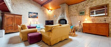 A cozy living room with a stone wall, wooden ceiling beams, a fireplace, and a television.