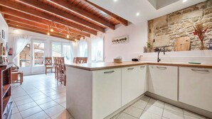 A kitchen with white cabinets, a wooden countertop, and a stone wall. There is a dining area with chairs and a table. - Stunning home in Chenac-Saint-Seurin-d' (Chenac-Saint-Seurin-d')