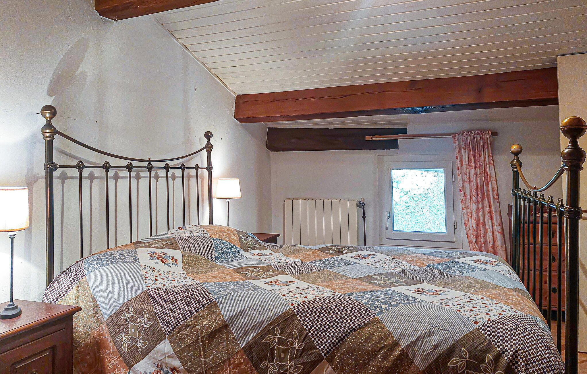 A bedroom with a metal bed frame, a quilted bedspread, a nightstand with a lamp, a radiator, and a window with curtains.