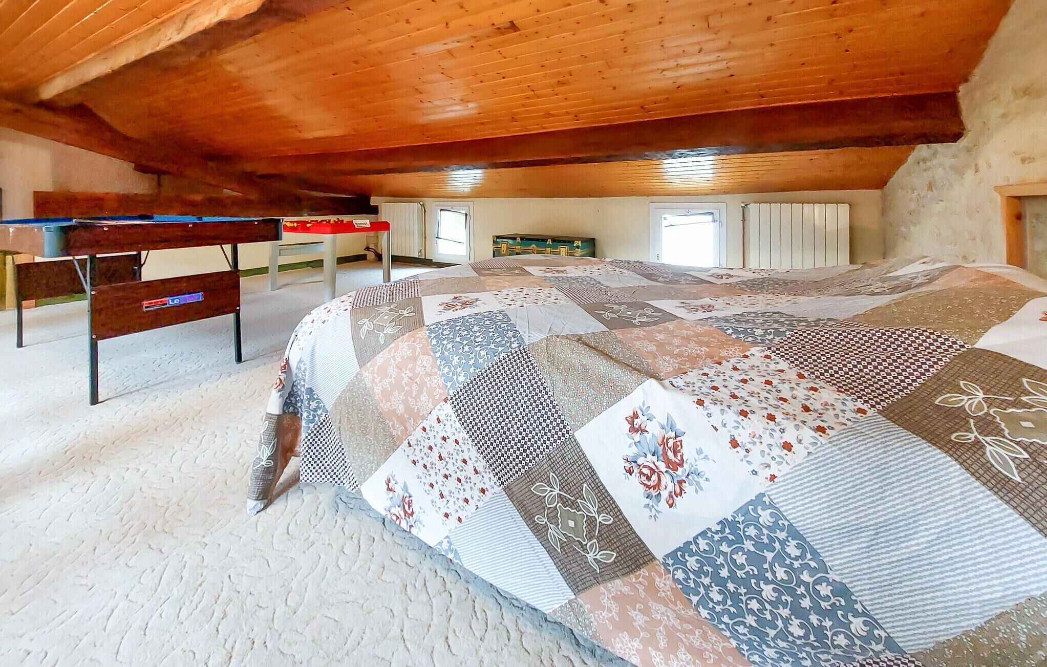 Un espacioso dormitorio en el ático con una cama grande, vigas de madera en el techo y un escritorio.