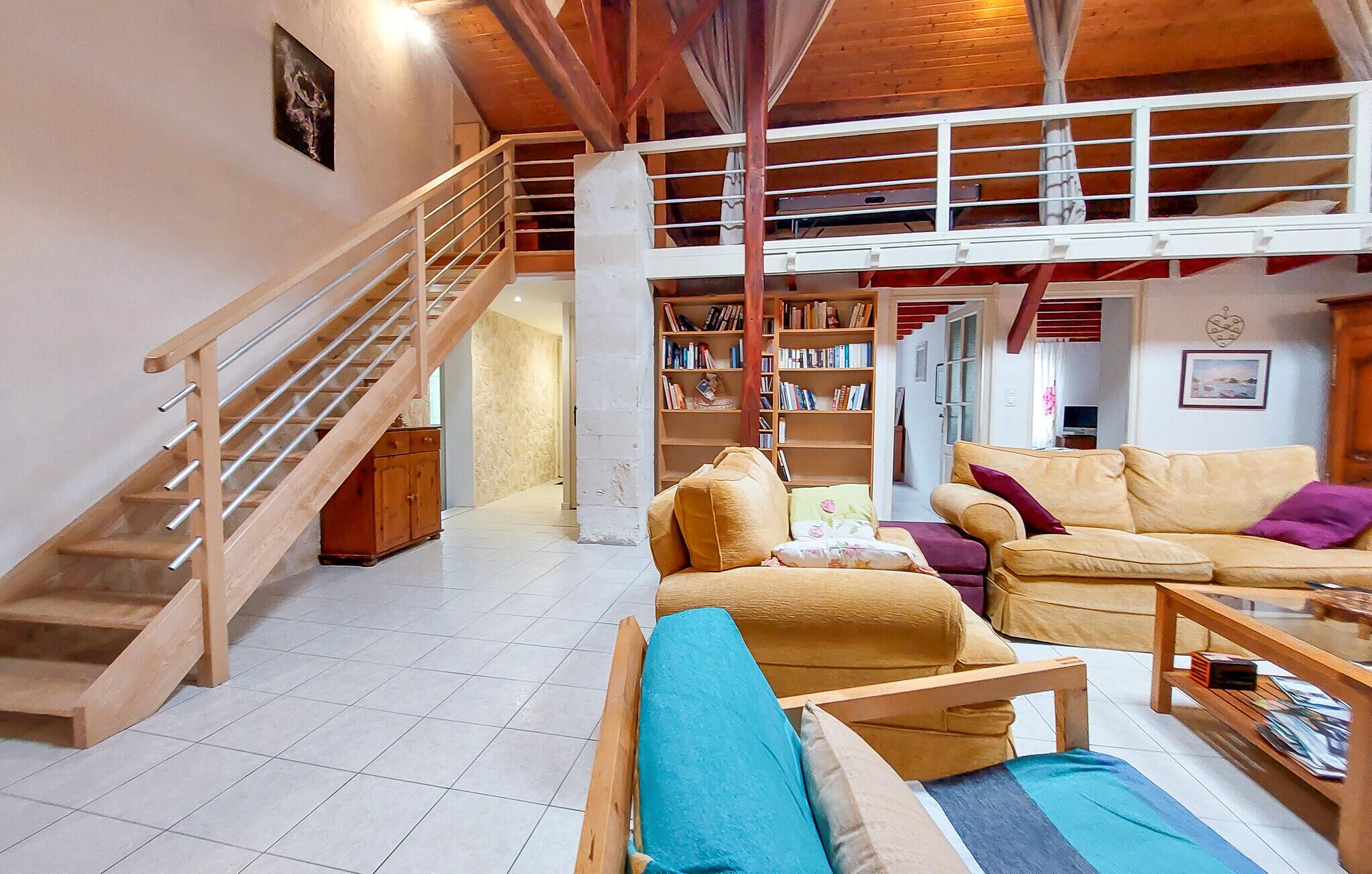 A spacious living area with a wooden staircase, a large bookshelf, and a yellow sofa.
