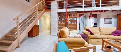A spacious living area with a wooden staircase, a large bookshelf, and a yellow sofa.