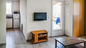 Ett litet, kompakt bostadsutrymme med ett minikök, en tv som är monterad på väggen, en träbänk och ett bord.