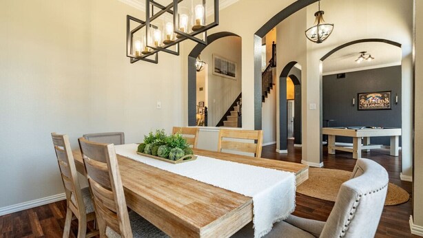 A dining area with a wooden table, chairs, and a decorative centerpiece. There is a billiards table and a sign in the background. - Designer-Styled Modern Farmhouse w/ Heated Pool (Allen)