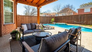 A covered patio with outdoor furniture, a pool, and a wooden fence. - Designer-Styled Modern Farmhouse w/ Heated Pool (Allen)