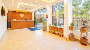 A hotel reception area with a wooden reception desk, a blue mat, and potted plants. - The Hosteller Lansdowne (Lansdowne)