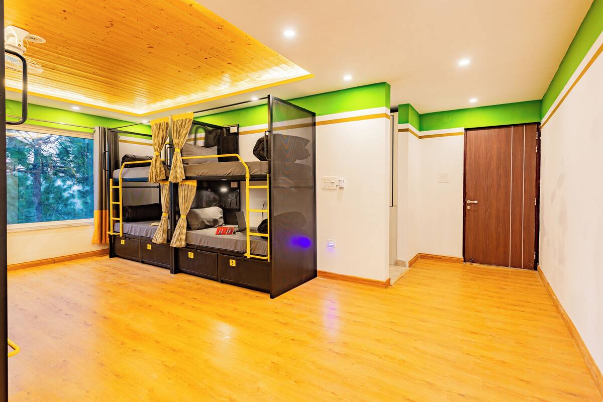 A room with bunk beds, a wooden floor, a window with a view of trees, and a door.