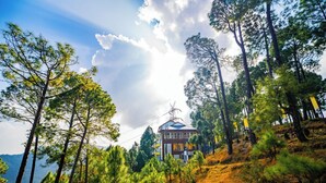 A mountain lodge with a prominent tower, surrounded by pine trees and a clear sky. - The Hosteller Lansdowne (Lansdowne)