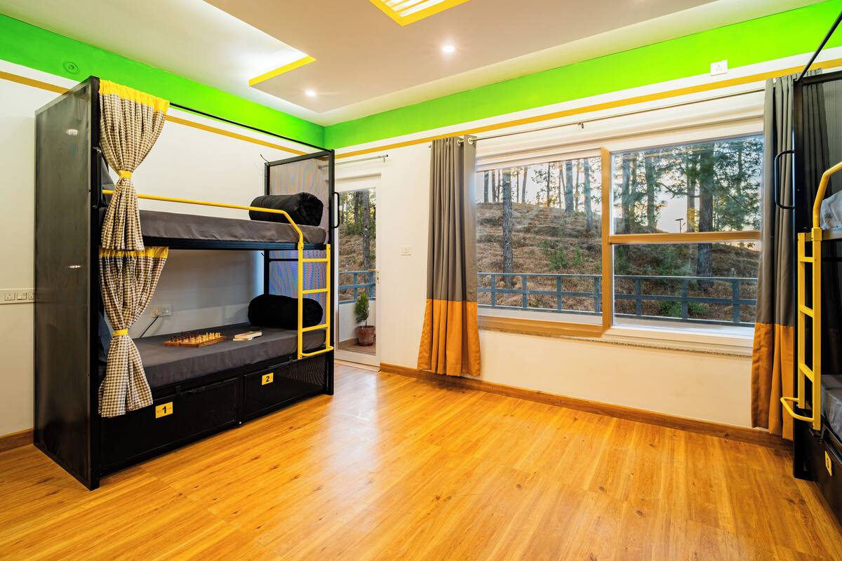 A room with bunk beds, a window with a view of trees, and a wooden floor.