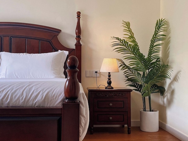 A neatly made bed with white linens, a wooden nightstand with a lamp, and a potted plant beside the bed. - Wanning 911 Surf Club (Wanning)